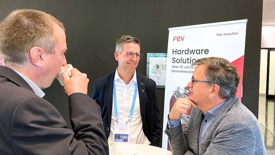 Three attendees in conversation at the FEV exhibition booth  at The Automotive Battery – Key Technology for Electric Vehicles 9th - 10th July 2025