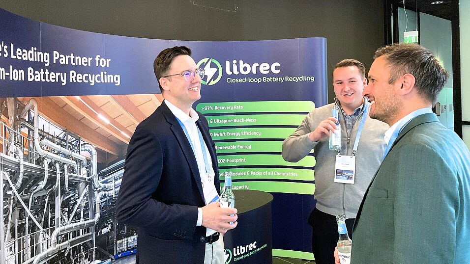 Three attendees smiling an enjoying conversation in front of the librec exhibition booth  at The Automotive Battery – Key Technology for Electric Vehicles 9th - 10th July 2025